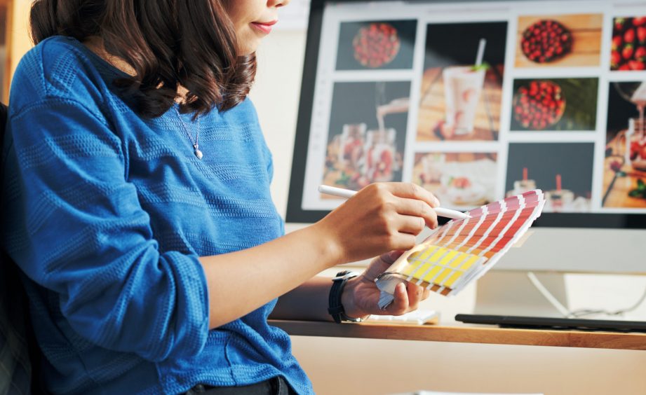 Close-up of Asian woman in blue sweater picking out palette for website design in modern office